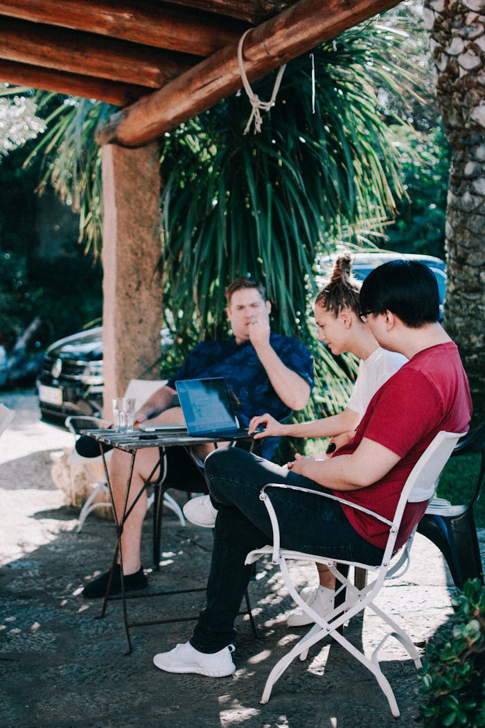 services-03 Three adults collaborating outdoors with laptops in a tropical setting.