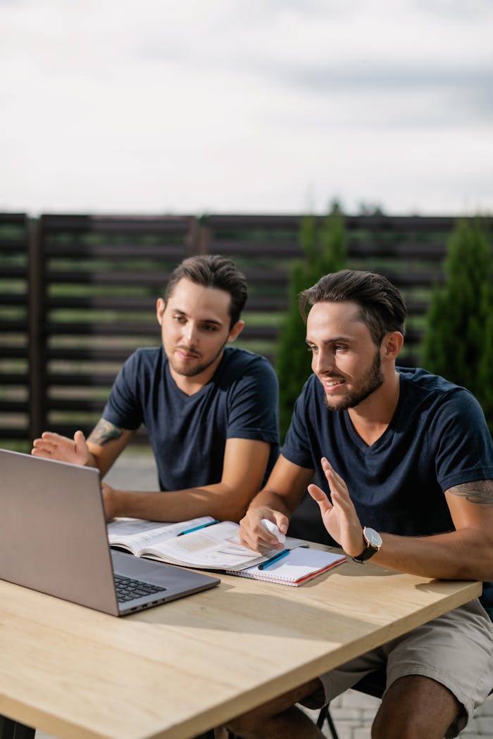 services-02 Two twin brothers engaging in online learning outdoors on a laptop.